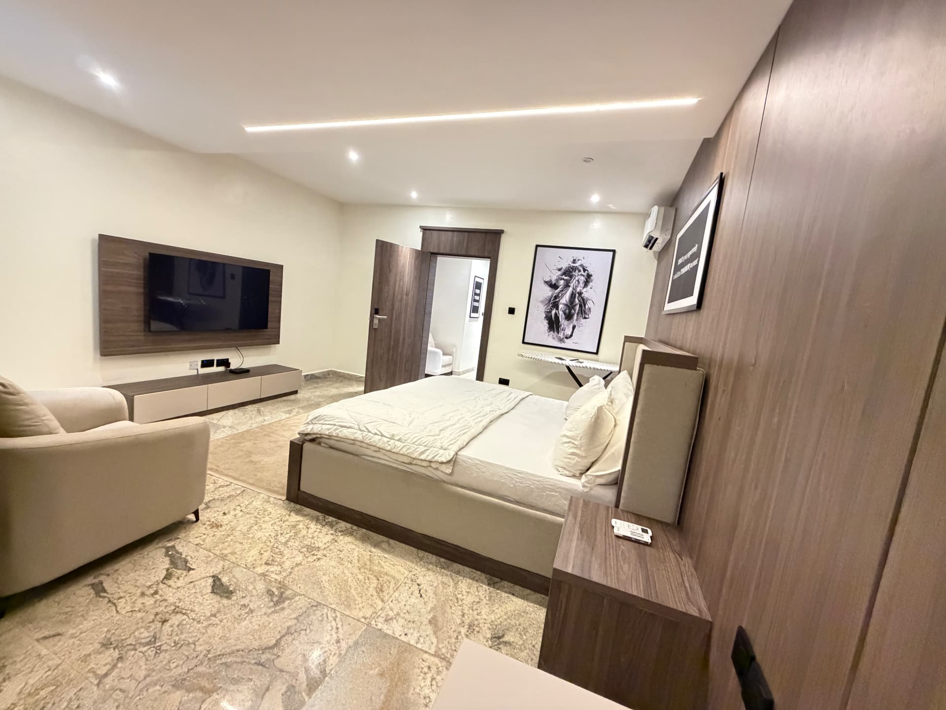 Wide view of the bedroom with double bed, armchair, wall-mounted television and wardrobe wall