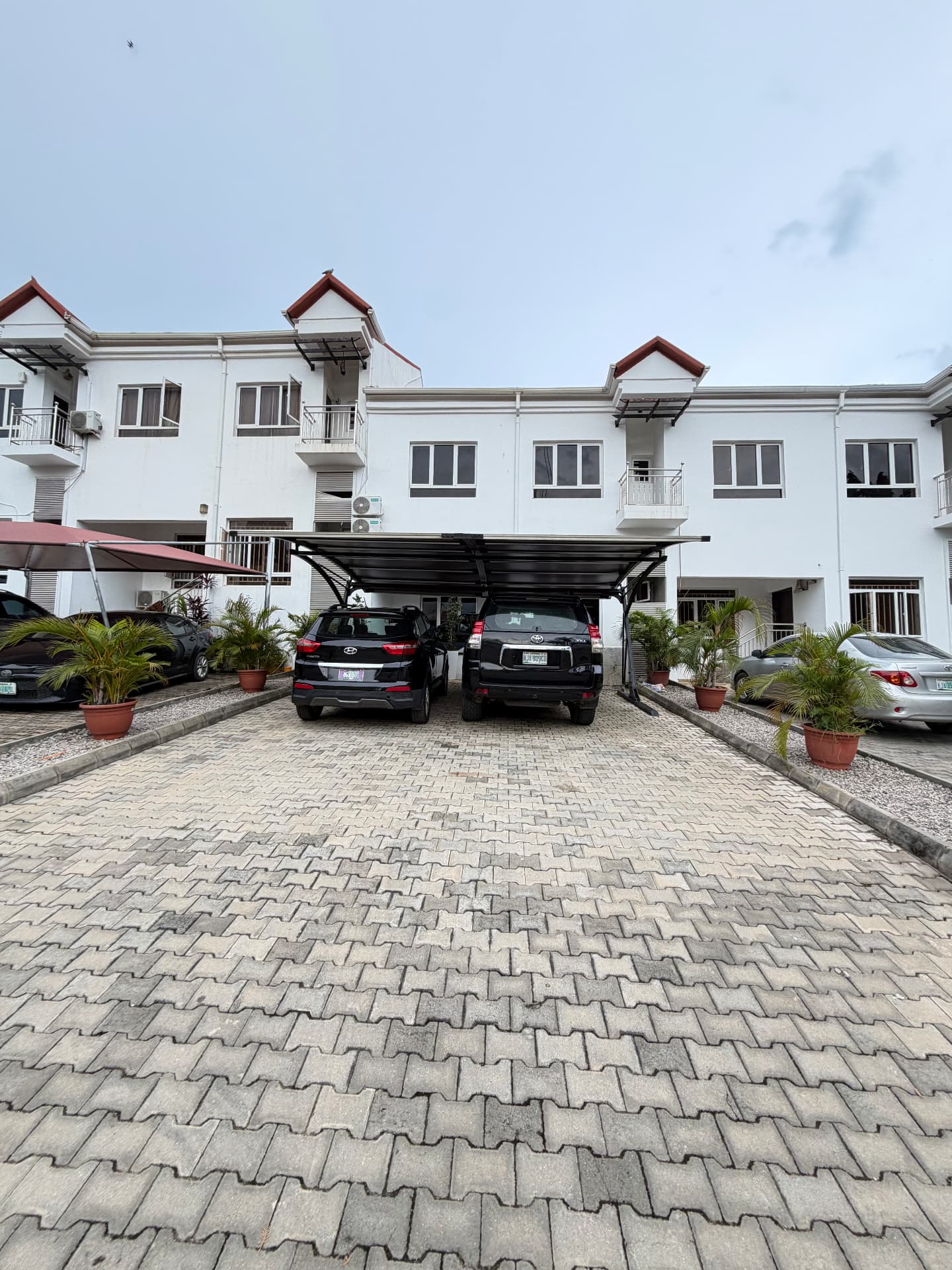 Paved residential driveway with covered parking in front of a white terraced residential block in Abuja