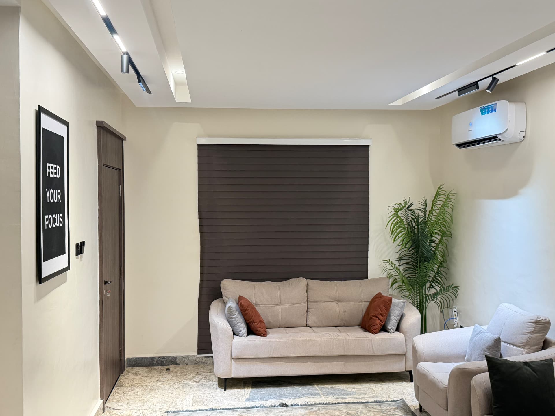 Living area with sofa, armchair, plant and window blind under recessed track lighting